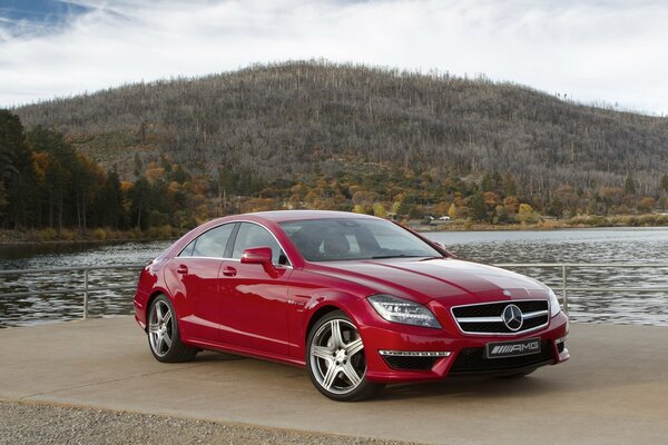 Sky, mountain, forest and red Mercedes CLS63 sedan on the lake shore