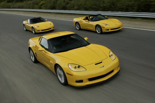 Three yellow Chevrolet Coupes are racing down the freeway