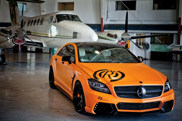 Mercedes naranja en un hangar de aviones contra un avión blanco