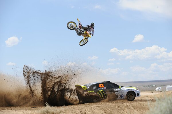 The stunt of a motorcyclist flying over a subaru moving on a wild highway