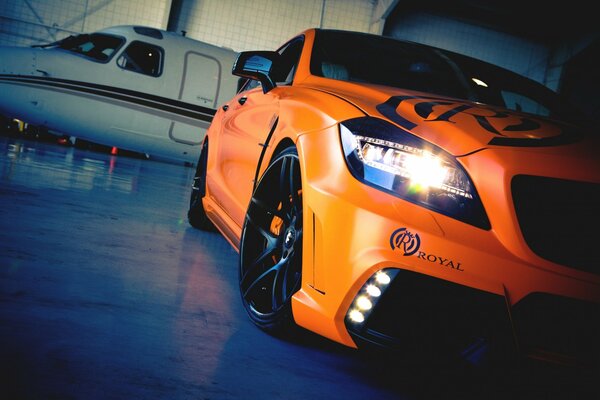 An orange car near a white plane