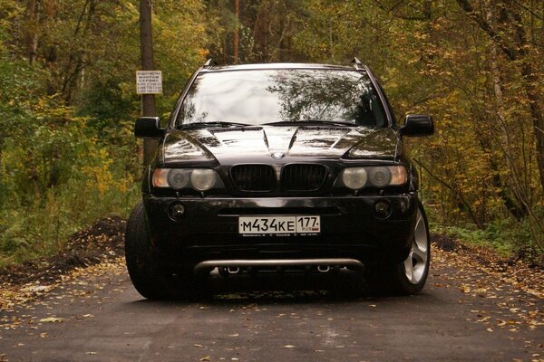 Black BMW on a forest path against the background of autumn trees