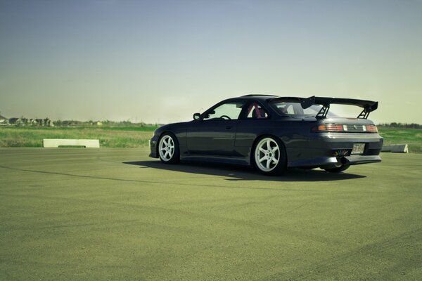 A black Nissan S14 stands driverless against an open space background