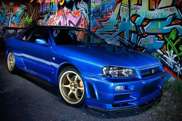 Niebieski Nissan zaparkował przy ścianie z graffiti