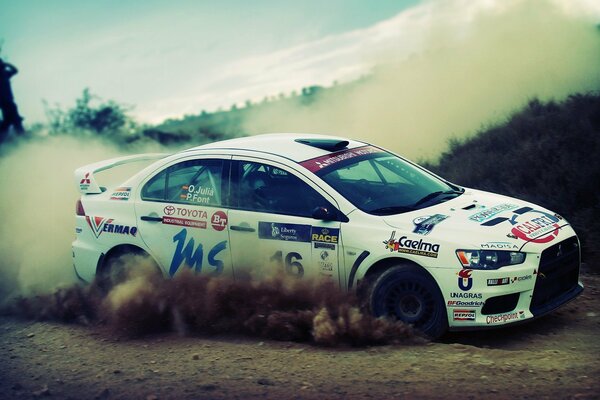 Une voiture de course de couleur blanche avec des autocollants passe une piste poussiéreuse