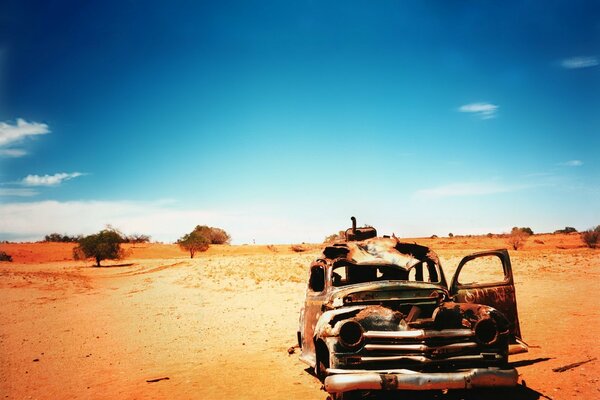 An old car in the middle of the desert against the sky