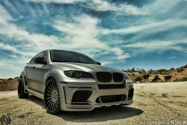 Gris hermoso BMW en la carretera contra un cielo azul nublado