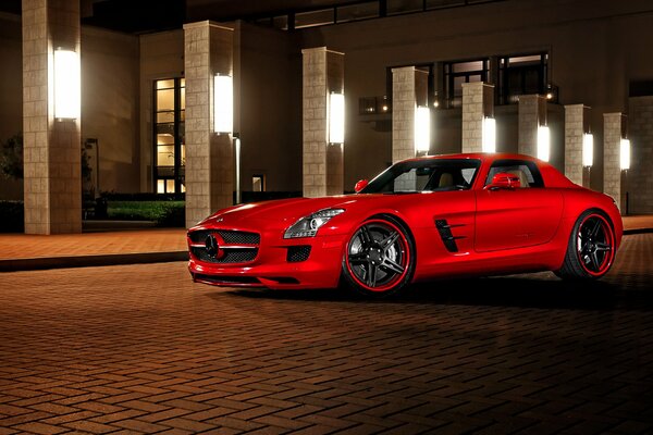 The image of a stylish red sports car on the background of a building with illumination in the evening