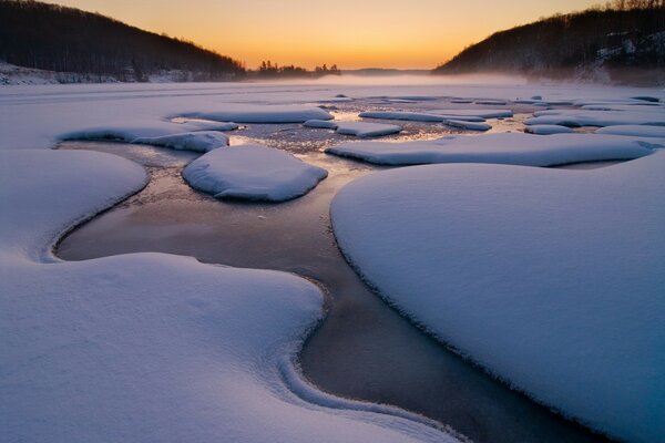 A stream surrounded by snow during sunset