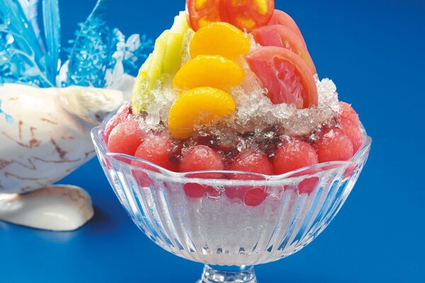 Fruit dessert in a transparent bowl on a leg on a blue background