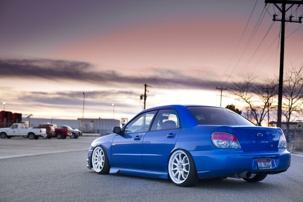 A blue car on the road against the background of sunset and a gray factory building