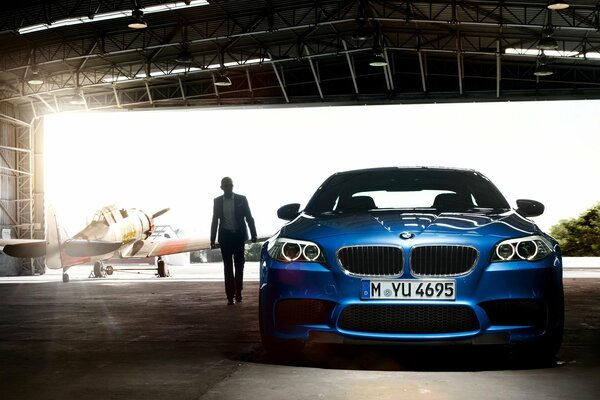 A blue bmw m5 stands in an airplane hangar