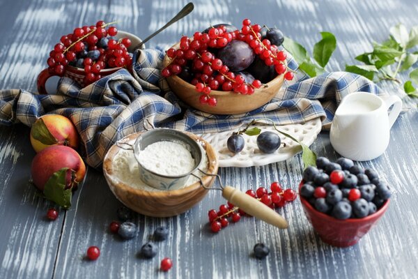 Äpfel, Blaubeeren und Johannisbeeren auf einem Tisch mit Mehl und Milch