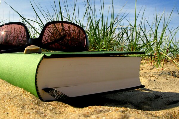 Brille auf einem Buch im Sand