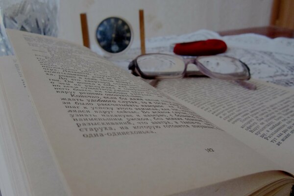 An open book with glasses on it and a clock on the background