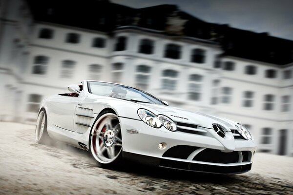 Sport-weißes Auto der Marke Mercedes in Bewegung vor dem Hintergrund eines dreistöckigen Gebäudes
