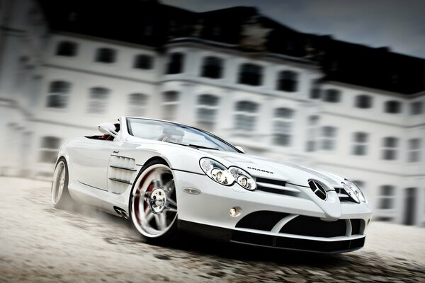 A sporty white Mercedes car in motion against the background of a three-storey building