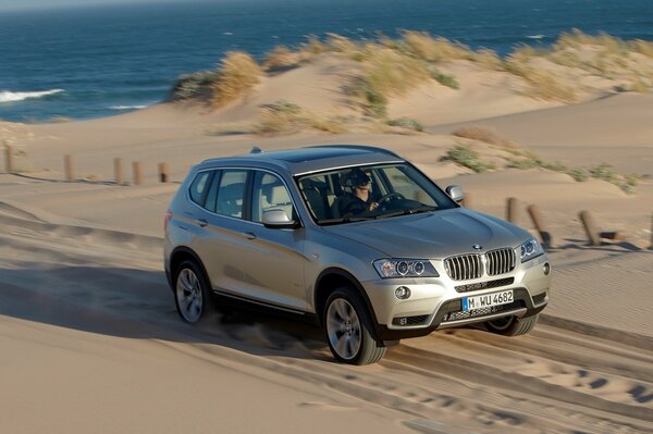 Une bmw X3 argentée roule sur le sable sur fond de mer