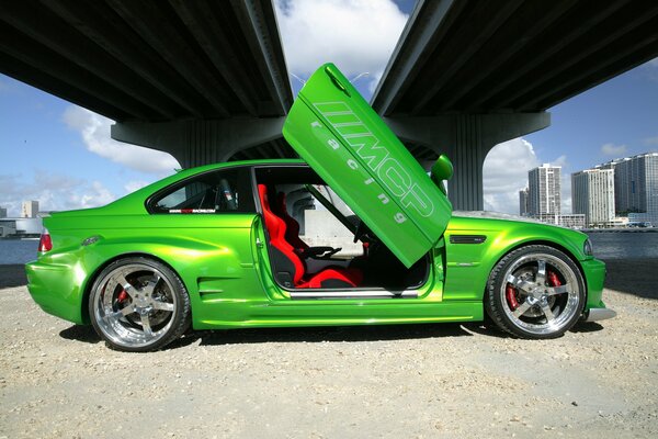 BMW verde con puertas Lambo abiertas debajo del puente en la ciudad