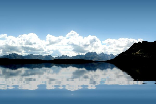 The water stands quietly on the lake reflecting clouds and mountains