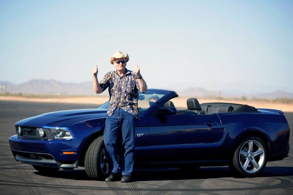 A man stands near a Ford Mustang convertible blue