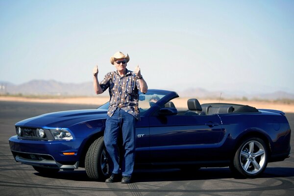 Uomo in piedi vicino a una Ford Mustang convertibile di colore blu