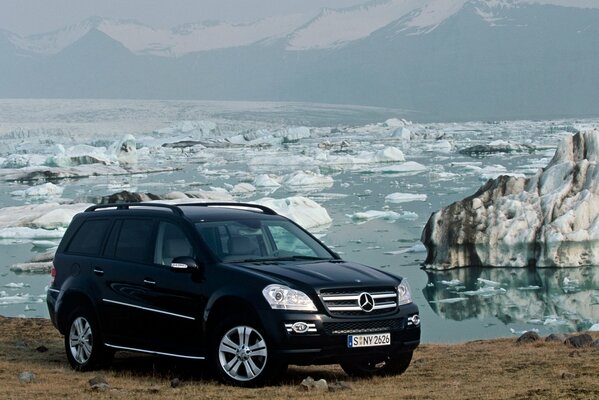 Un SUV Mercedes noir sur la rive d un réservoir avec de la glace fondante et des montagnes au loin