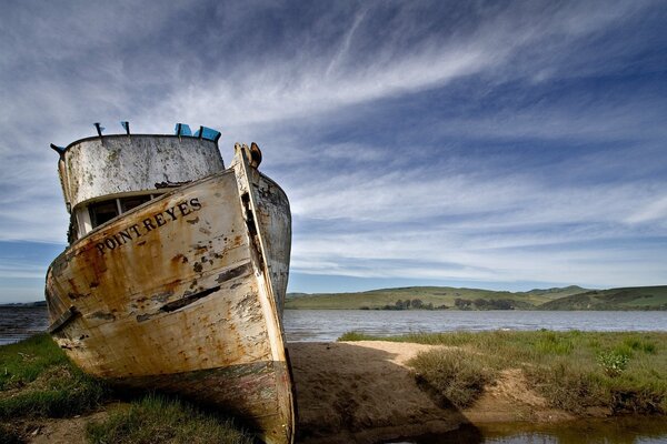 An old ship on the shore under a blue sky