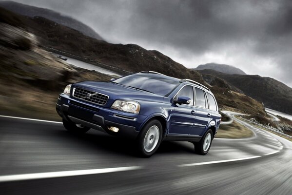 A blue Volvo is driving on a deserted road