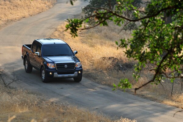 A pickup truck is driving on a mountain road against a background of yellow grass