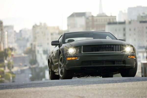 Ford mustang bullitt corre por la carretera en medio de edificios de gran altura de la ciudad