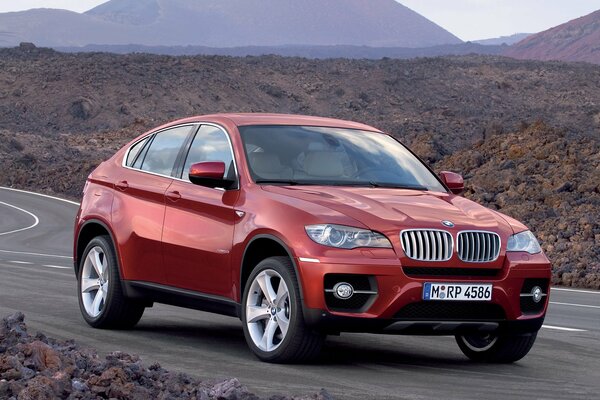 Voiture BMW rouge sur la route dans un terrain rocheux sur fond de montagnes