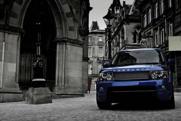 A cool blue car on the road among gray houses