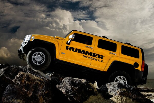 Hummer yellow on rocks against a background of clouds