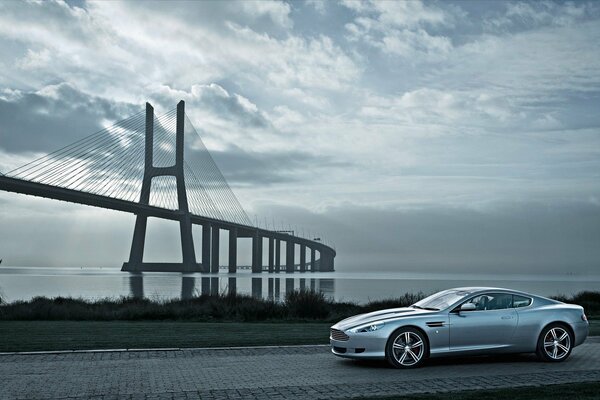 Against the background of the river and the bridge - a silver Aston Martin