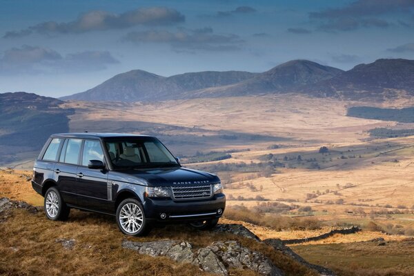 Чёрный Range Rover стоит на увесистом утесё на фоне красивой долины