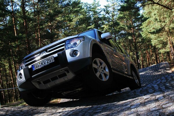 A silver car driving on uneven cobblestones