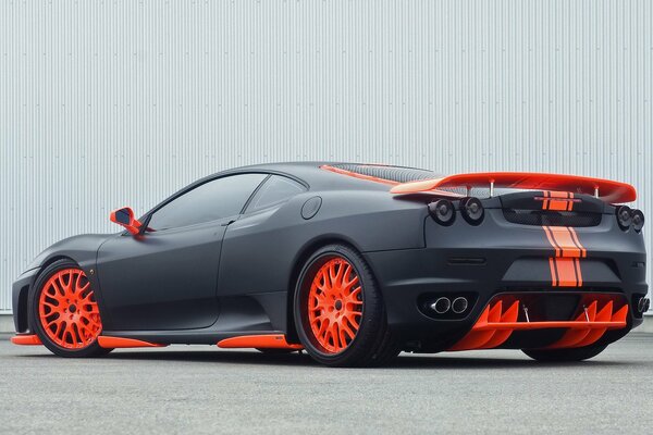 A black and red Ferrari stands near the fence