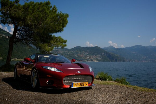 A sporty red spider car stands against the background of water