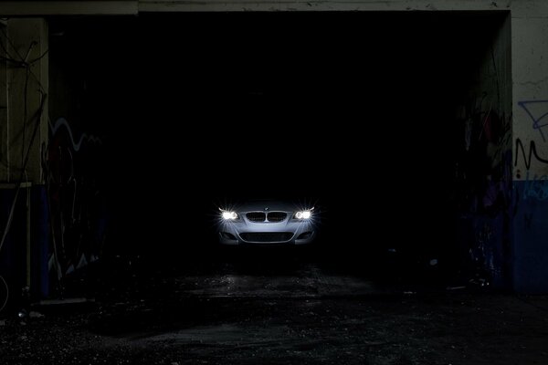 A grey bmw coming out of the dark with its headlights on