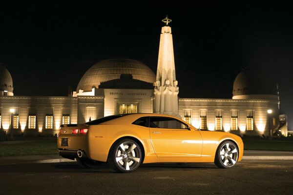 A yellow Chevrolet car at night outside the building