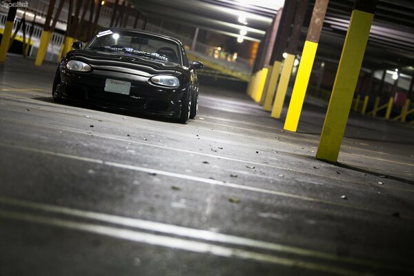 A black sporty low Mazda rides in a night parking lot