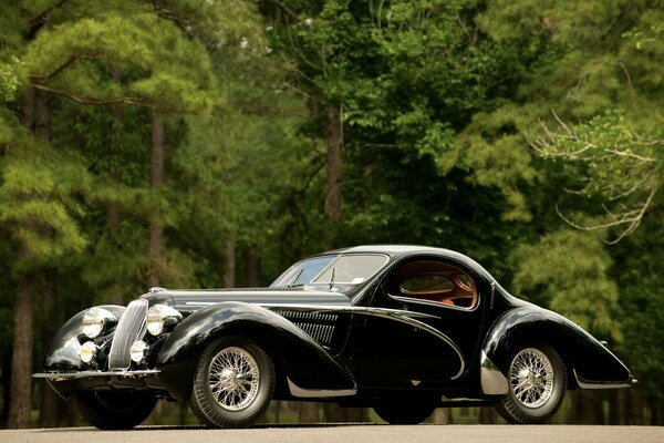 Black retro car on the road in the forest