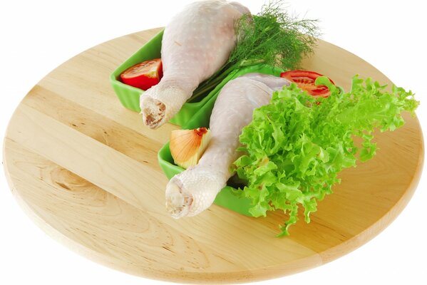 Dwie udka z kurczaka w tacach z warzywami na okrągłej desce