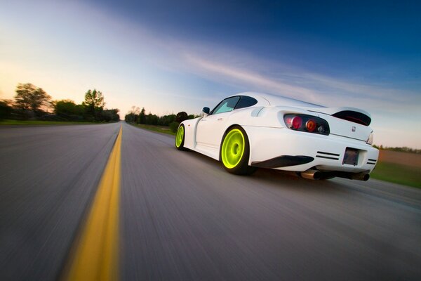 A white Honda with green wheels rushes along the highway