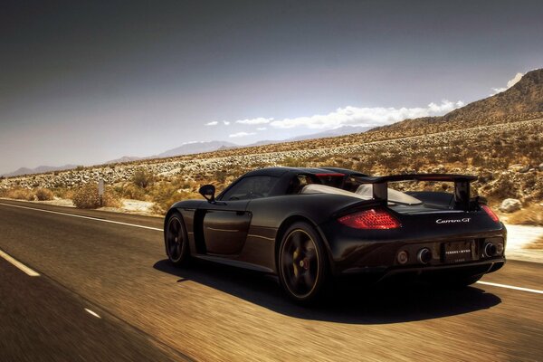 Porsche carrera черного цвета на дороге в прериях