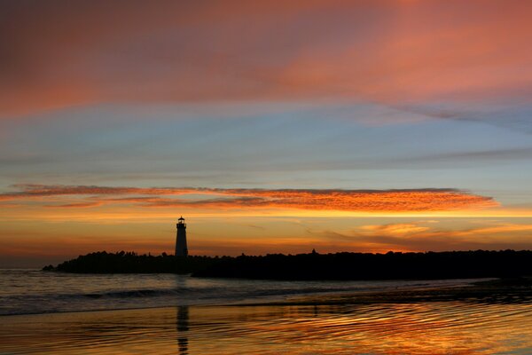 The lighthouse is reflected in the water against the background of the orange sky flooded with sunset