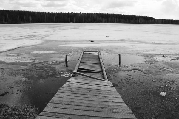 Antiguo puente de pescadores en un estanque congelado con vistas al bosque en blanco y negro