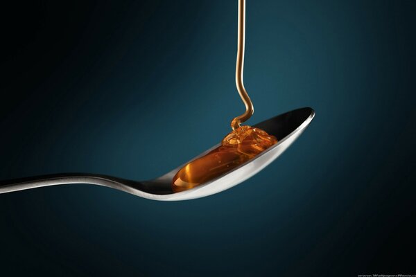 A teaspoon on a gray background is a trickle of honey