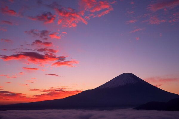 A mountain against a background of scarlet clouds, the foot of which is shrouded in fog